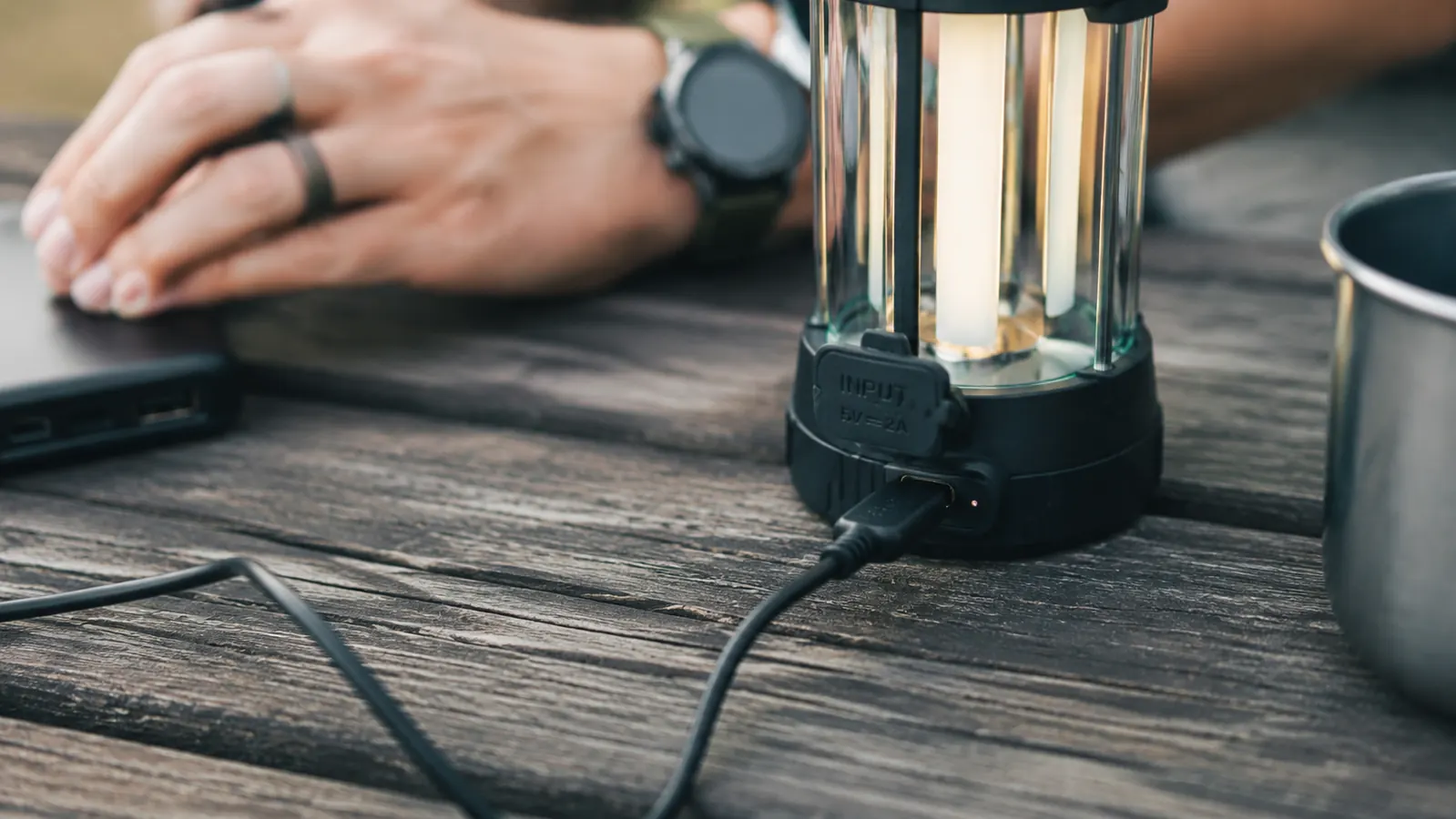 Campsite at night with rechargeable lantern on a table illuminating a camp kitchen setup, forest dark beyond