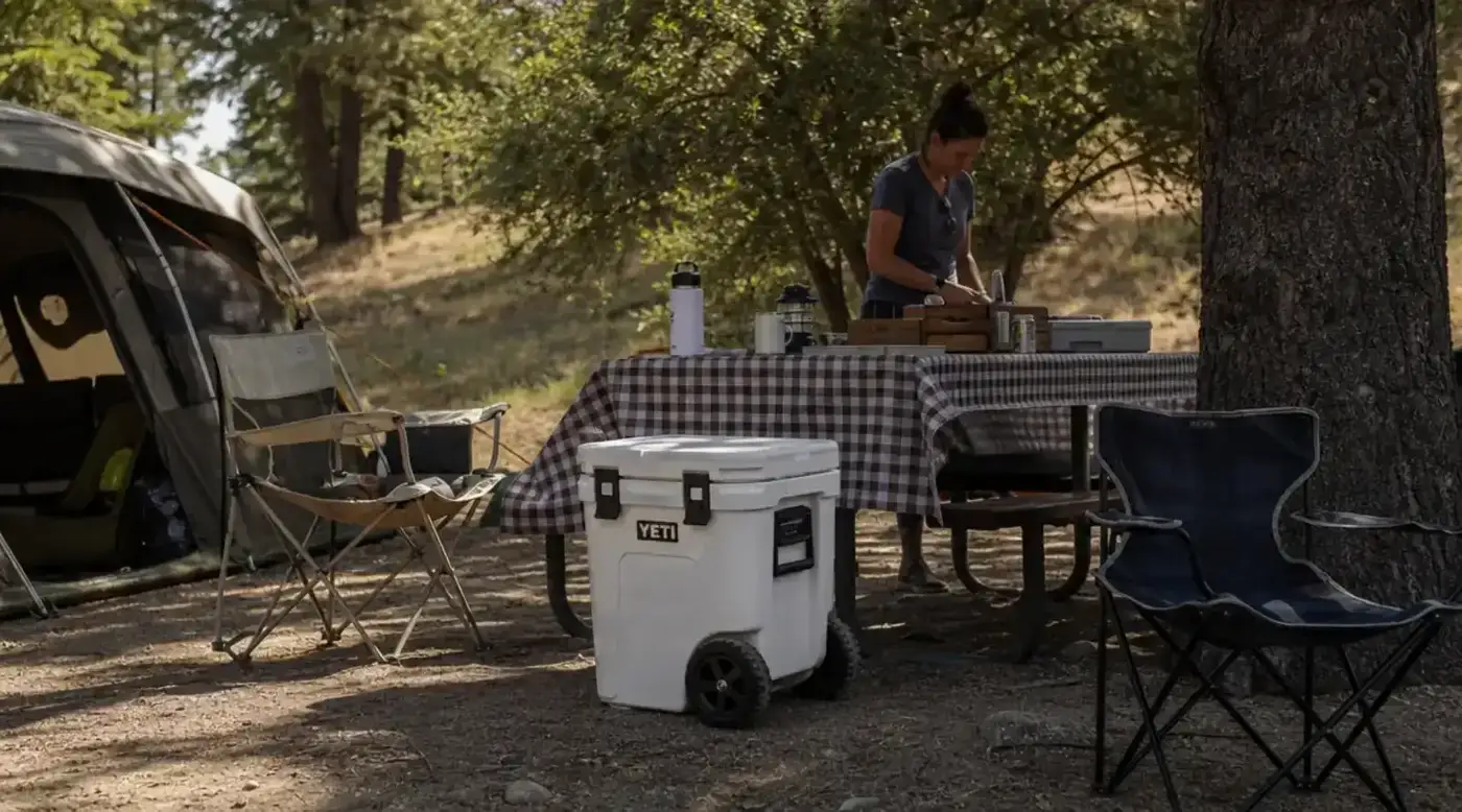 Campsite from above showing organized gear including rolling cooler beside a picnic table with stove and lantern